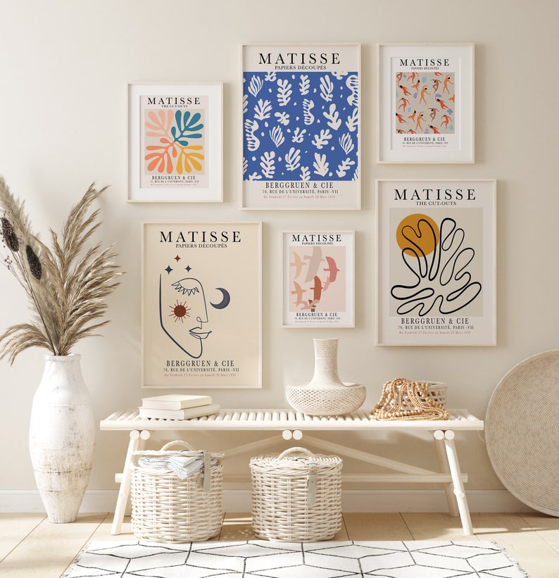 May include: Five framed art prints with a white background and black text. The prints feature colorful abstract designs and the text "MATISSE" and "PAPIERS D&Eacute;COUP&Eacute;S". The prints are hanging on a white wall above a white bench with two wicker baskets.