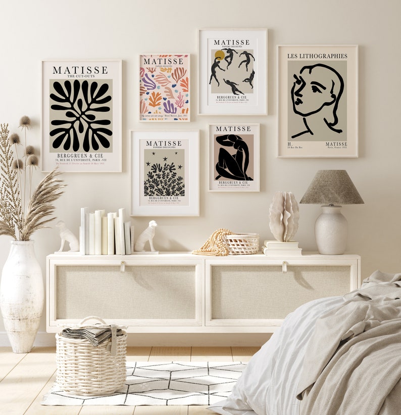 May include: A set of six black and white Matisse art prints with a minimalist design. The prints feature abstract shapes, figures, and floral motifs. The prints are framed in white and arranged on a white wall above a white dresser.