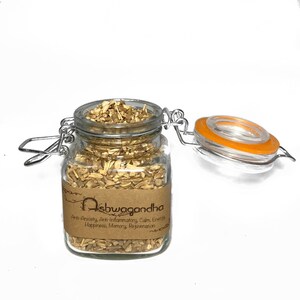 May include: A glass jar with a metal clasp lid filled with dried ashwagandha root. The jar has a brown label with the text "Ashwagandha" and a list of benefits: Anti-Anxiety, Anti-Inflammatory, Calm, Energy, Happiness, Memory, Rejuvenation.