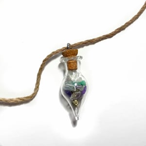 May include: A glass bottle pendant with a cork stopper filled with various colorful crystals, including amethyst, clear quartz, green aventurine, and pyrite. The bottle is attached to a brown twine cord.