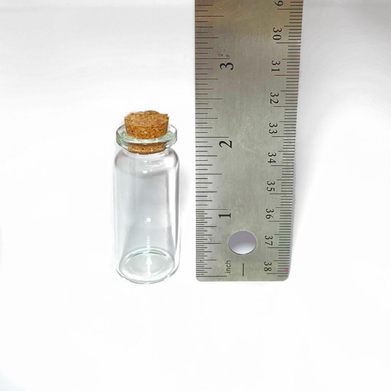 Peut inclure: Une bouteille en verre transparent avec un bouchon en li&egrave;ge, mesurant environ 5 cm de haut. La bouteille est &agrave; c&ocirc;t&eacute; d'une r&egrave;gle pour r&eacute;f&eacute;rence de taille.