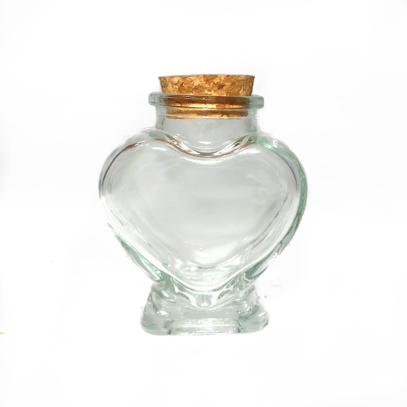 May include: A clear glass heart-shaped bottle with a cork stopper. The bottle is empty and has a smooth, rounded surface.