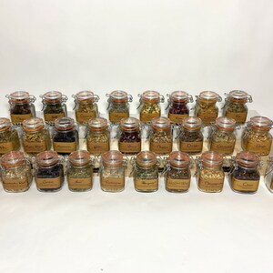Puede incluir: Una colecci&oacute;n de 30 peque&ntilde;os frascos de vidrio con tapas de corcho, llenos de diversas hierbas y especias secas. Los frascos est&aacute;n dispuestos en filas sobre una superficie de madera.