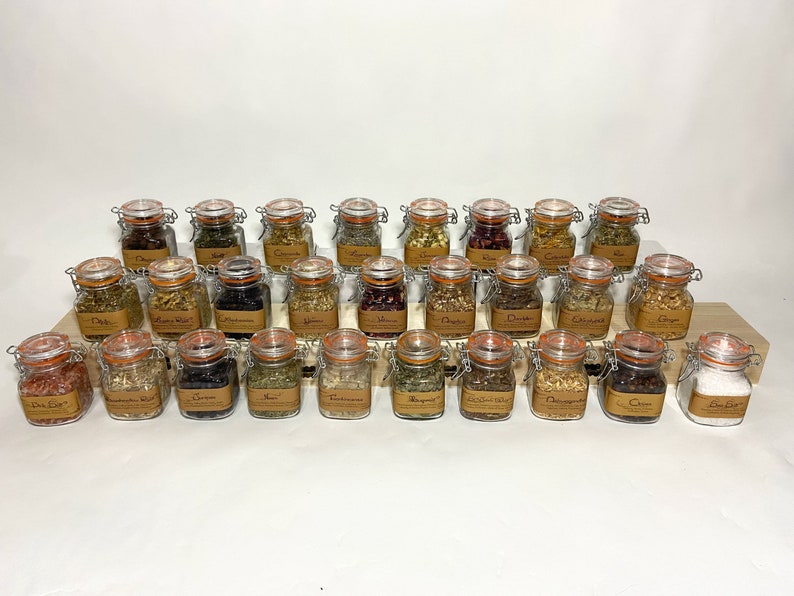 Puede incluir: Una colecci&oacute;n de 30 peque&ntilde;os frascos de vidrio con tapas de corcho, llenos de diversas hierbas y especias secas. Los frascos est&aacute;n dispuestos en filas sobre una superficie de madera.