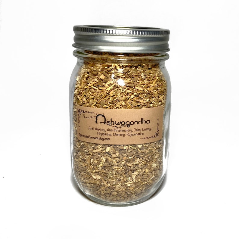 May include: A glass jar filled with dried ashwagandha root. The jar has a brown label with the text "Ashwagandha" and a list of benefits: Anti-Anxiety, Anti-Inflammatory, Calm Energy, Happiness, Memory, Rejuvenation. The website address "SpiritValeConnect.stay.com" is printed on the label.