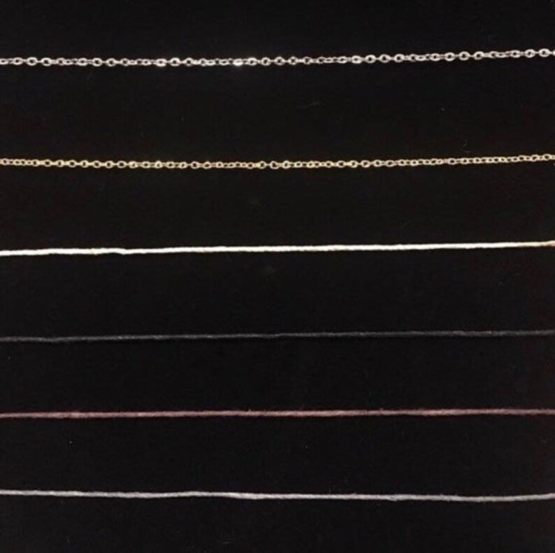 Op de afbeelding: Een close-up van zes verschillende soorten kettingen, waaronder zilver, goud, wit, zwart, bruin en wit. De kettingen zijn in rijen op een zwarte achtergrond gerangschikt.