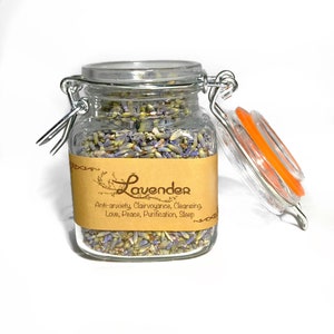 Peut inclure: Un bocal en verre avec un couvercle à fermoir métallique rempli de fleurs de lavande séchées. Le bocal porte une étiquette en papier brun sur laquelle est inscrit "Lavender" et les bienfaits de la lavande : "Anti-anxiété, Clairvoyance, Nettoyage, Amour, Paix, Purification, Sommeil".