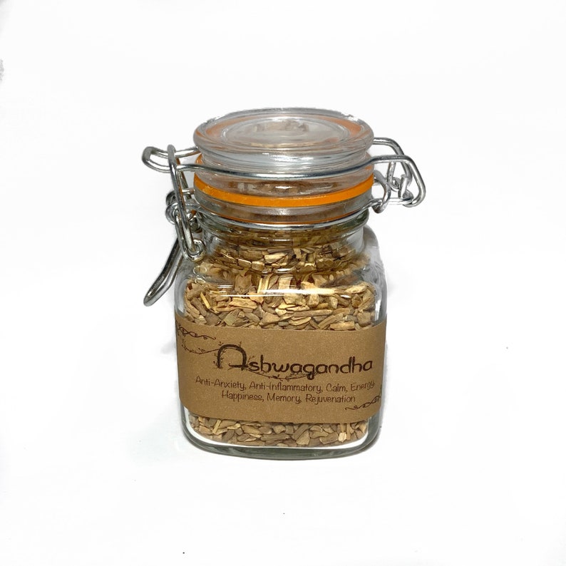 May include: A glass jar with a metal clasp lid filled with dried ashwagandha root. The jar has a brown paper label with the text "Ashwagandha" and a list of benefits: Anti-Anxiety, Anti-inflammatory, Calm, Energy, Happiness, Memory, Rejuvenation.