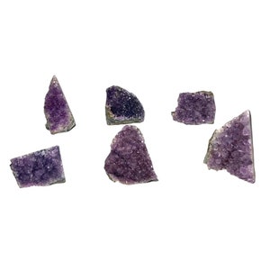 May include: Six small amethyst crystal clusters, each with a different shape and size, are arranged on a white background. The crystals are a deep purple colour and have a rough, natural texture.