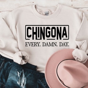 May include: A beige sweatshirt with the text "CHINGONA EVERY. DAMN. DAY." printed in black.