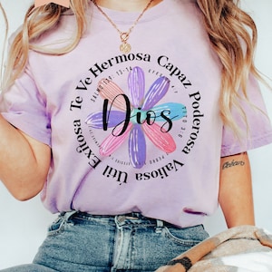 Puede incluir: Una camiseta morada con un dise&ntilde;o floral y el texto "Te Ve Hermosa Capaz Dios Poderosa Valiosa Util Exitosa" con vers&iacute;culos b&iacute;blicos alrededor del texto.