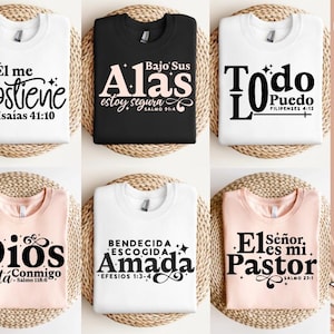 Könnte beinhalten: Sechs T-Shirts in Weiß, Schwarz und Pfirsich, jeweils mit einem anderen spanischen religiösen Zitat in schwarzer Schrift. Die Shirts zeigen Sätze wie "Sostiene" und "Todo Puedo". Das Bild enthält auch das Wort "RELIGION" und die Zahl "15".