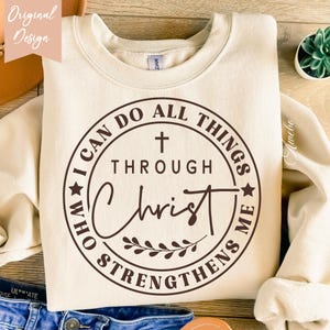 May include: A beige sweatshirt with a brown circle graphic that says "I can do all things through Christ who strengthens me". The graphic also includes a cross and a wreath.