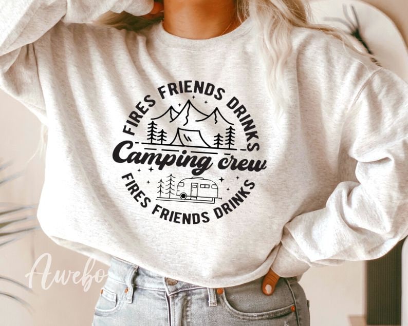K&ouml;nnte beinhalten: Ein wei&szlig;er Pullover mit einem schwarzen Grafikdesign, auf dem "Fires Friends Drinks Camping Crew Fires Friends Drinks" mit einer Bergszene und einem Wohnmobil steht.