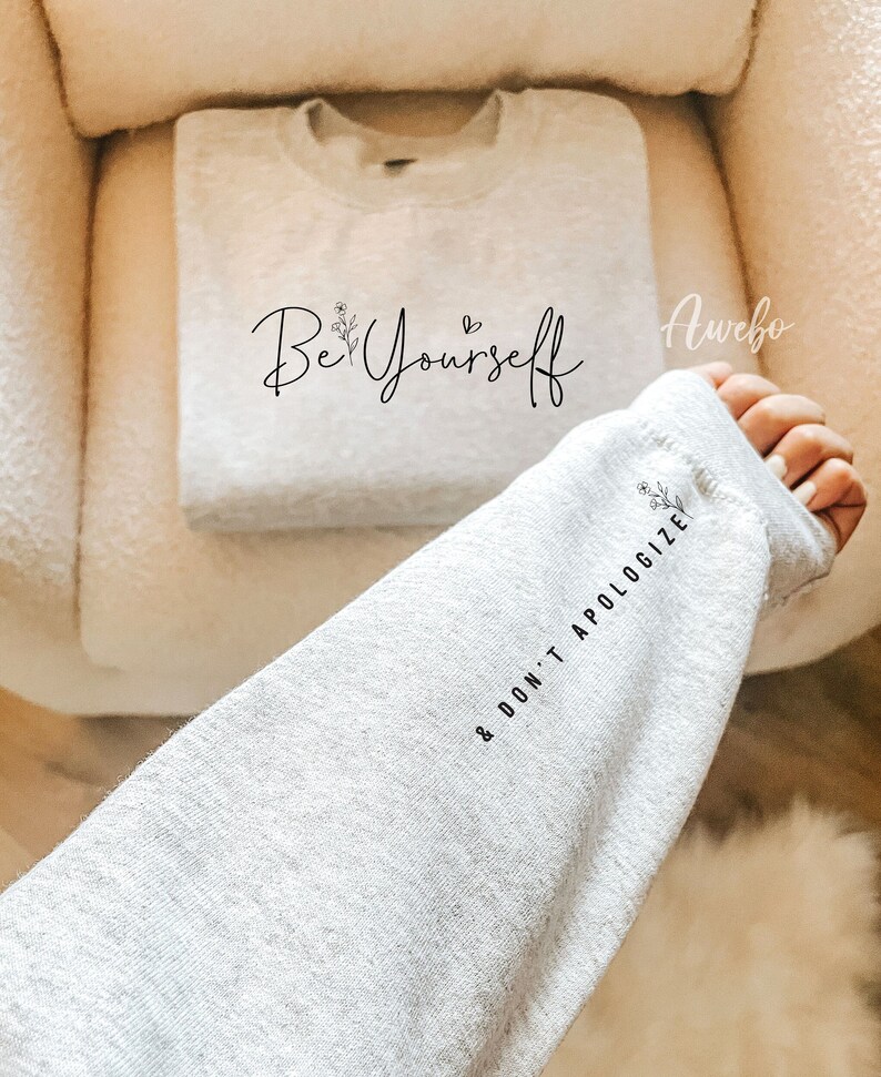 May include: Gray sweatshirt with the text "Be Yourself & Don't Apologize" and a small floral design. The text is in black and the floral design is in white.