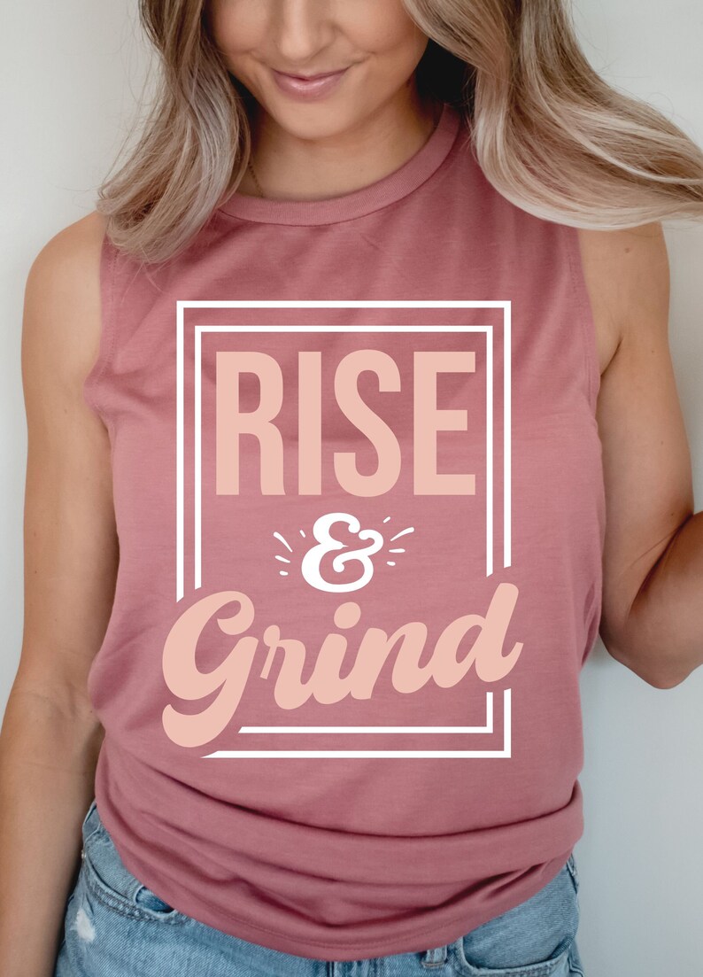 Pode incluir: Uma camiseta rosa sem mangas com o texto "RISE & Grind" em uma caixa branca.