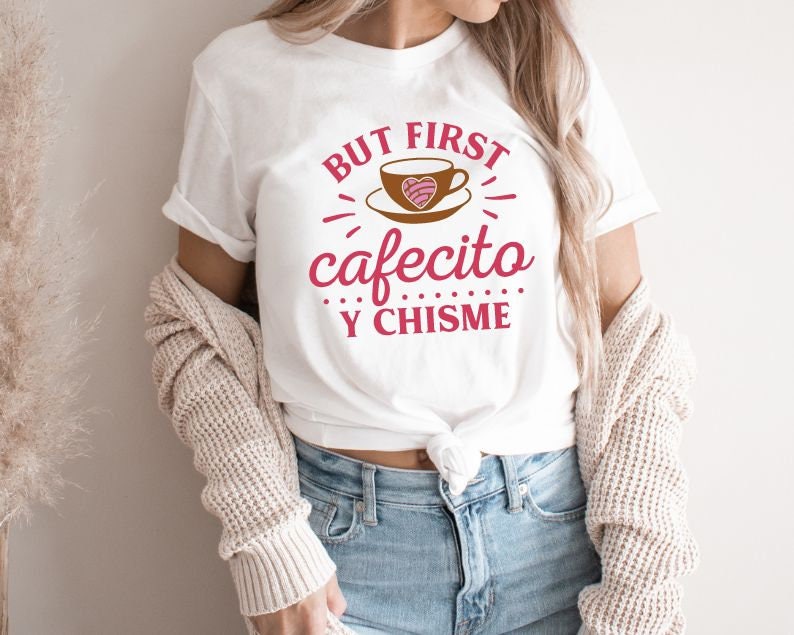 May include: White t-shirt with the text "But first, cafecito y chisme" in pink and brown lettering. The text is surrounded by a stylized coffee cup with a heart design.