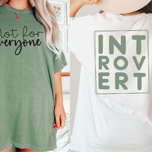 May include: Two t-shirts with different designs. The green t-shirt has the text "not for everyone" printed on the front. The white t-shirt has the word "INTROVERT" printed on the back in a green box.