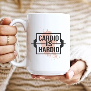 Pode incluir: Caneca de cer&acirc;mica branca com um gr&aacute;fico preto e branco que diz "Cardio is Hardio" com um gr&aacute;fico de barra. O gr&aacute;fico est&aacute; sobre um fundo de aquarela rosa.