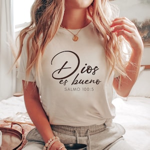May include: White t-shirt with the text "Dios es bueno" and "Salmo 100:5" in black cursive lettering.
