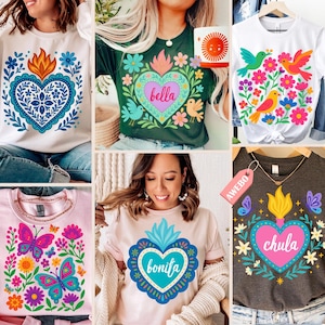 May include: Collection of graphic t-shirts featuring colorful heart and floral designs. The shirts include text such as "Bella", "Bonita", and "Chula". Designs include butterflies, birds, and suns. The shirts are in various colors, including white, pink, and dark grey.
