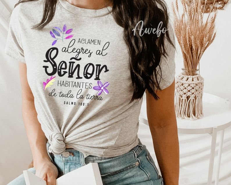 Puede incluir: Una camiseta gris con un gr&aacute;fico negro que dice "Aclamen alegres al Se&ntilde;or Habitantes de toda la tierra Salmo 100:1" con flores moradas y amarillas que rodean el texto.