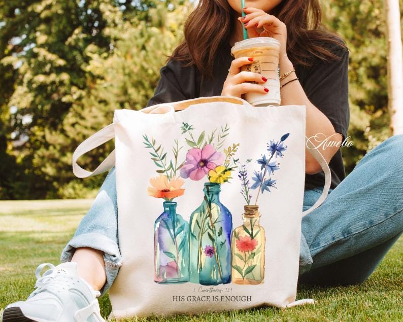 May include: White canvas tote bag with a floral design and the text "His Grace is Enough" and a scripture reference. The bag features three blue glass bottles with watercolour flowers.