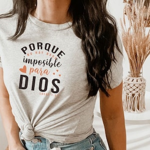 May include: Gray t-shirt with the text "PORQUE NO HAY NADA IMPOSIBLE PARA DIOS LUCAS 1:37" in black with a peach heart above the word "para" and two peach hearts to the right of the word "DIOS".