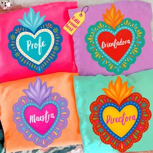 May include: Four colorful throw pillows with heart-shaped designs. Each pillow features a different color: pink, purple, orange, and teal. The hearts are decorated with floral patterns and the words "Profe", "Orientadora", "Maestra", and "Directora".