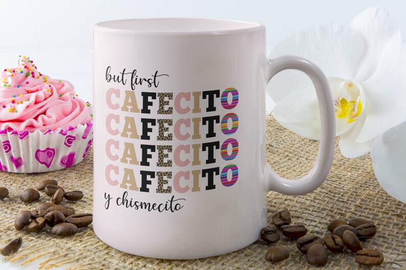 Puede incluir: Una taza de caf&eacute; de cer&aacute;mica rosa con el texto "but first cafecito y chismecito" en negro. La palabra "cafecito" se repite cuatro veces, cada una con un patr&oacute;n colorido diferente.