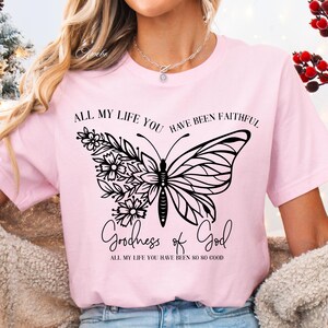 May include: Pink t-shirt with a black butterfly design and the text "ALL MY LIFE YOU HAVE BEEN FAITHFUL Goodness of God ALL MY LIFE YOU HAVE BEEN SO SO GOOD"