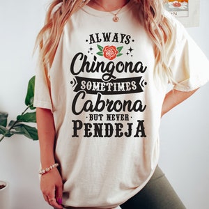 Puede incluir: Una camiseta blanca con un gr&aacute;fico negro que dice "Always Chingona Sometimes Cabrona But Never Pendeja" con una rosa roja en el medio.