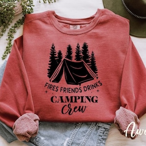 K&ouml;nnte beinhalten: Ein roter Pullover mit einem schwarzen Aufdruck einer Zelt, B&auml;umen und dem Text "Fires Friends Drinks Camping Crew".