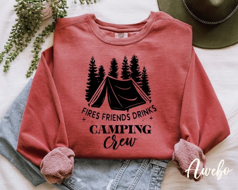 K&ouml;nnte beinhalten: Ein roter Pullover mit einem schwarzen Aufdruck einer Zelt, B&auml;umen und dem Text "Fires Friends Drinks Camping Crew".