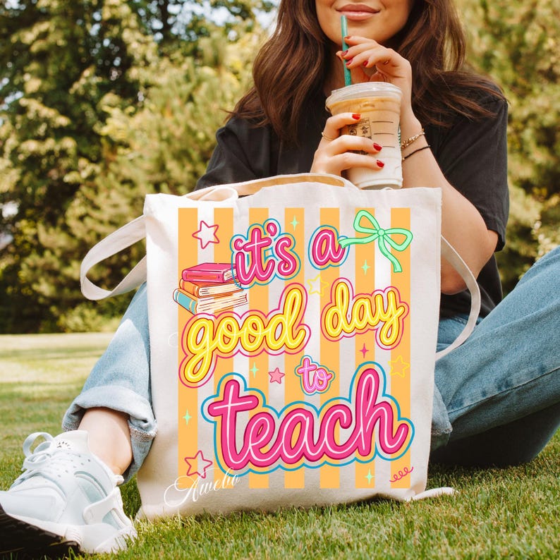 May include: Cream-colored tote bag with the text "it's a good day to teach" in pink and yellow. The bag has orange vertical stripes and a graphic of books. The bag has white handles.