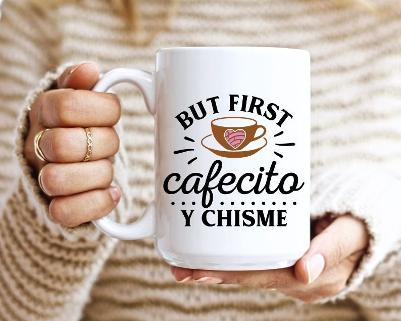 May include: White ceramic mug with black text that reads "But first cafecito y chisme". The mug has a brown illustration of a coffee cup with a pink heart-shaped pastry inside.