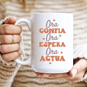 May include: White ceramic mug with the text "Ora Confia Ora Espera Ora Actua" in orange and brown lettering.