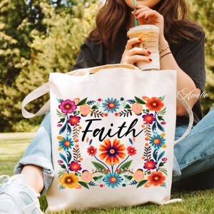 May include: A white canvas tote bag with a floral design and the word "Faith" in black lettering. The bag has a long strap and is being held by a person.