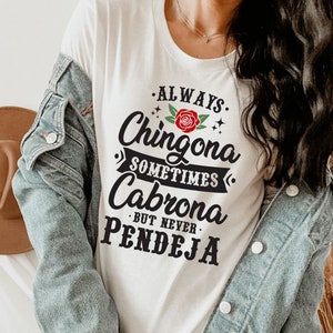 Puede incluir: Camiseta blanca con texto negro que dice "Always Chingona Sometimes Cabrona But Never Pendeja". Una rosa roja con hojas verdes est&aacute; por encima de la palabra "Chingona".