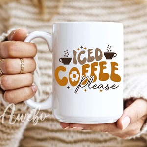 Może przedstawiać: Biały kubek ceramiczny z brązowo-pomarańczowym wzorem z napisem "Iced Coffee Please". Kubek ma mały kwiatek i ilustracje filiżanek do kawy.