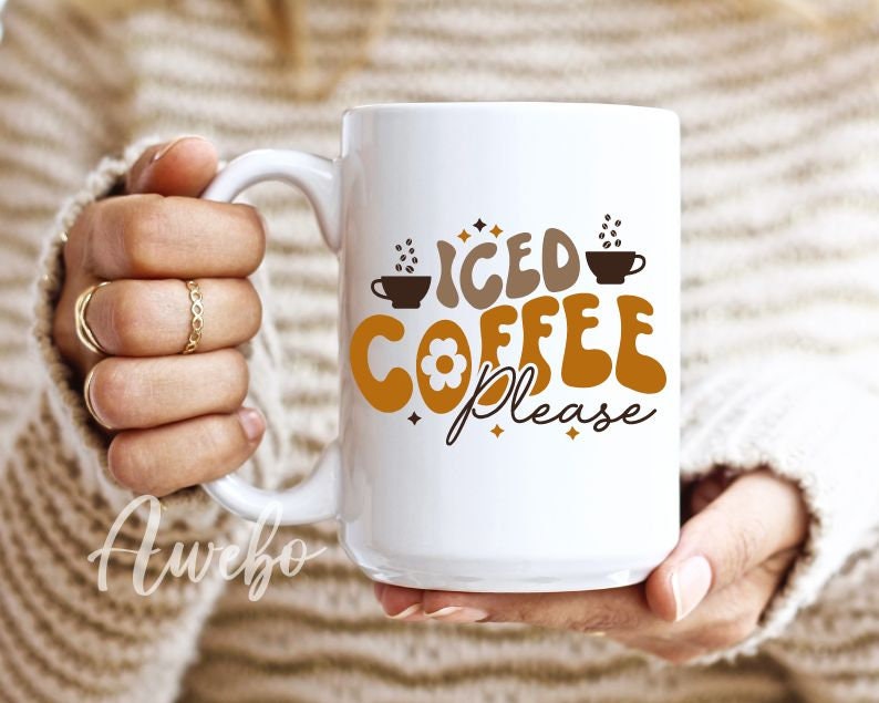 Może przedstawiać: Biały kubek ceramiczny z brązowo-pomarańczowym wzorem z napisem "Iced Coffee Please". Kubek ma mały kwiatek i ilustracje filiżanek do kawy.