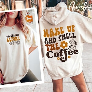 Może przedstawiać: Dwie białe koszulki z nadrukiem o tematyce kawy. Jedna koszulka ma napis "No Talkie Before Coffee" z grafiką kubka z kawą. Druga koszulka ma napis "Wake Up and Smell the Coffee" z grafiką kubka z kawą i kwiatem.