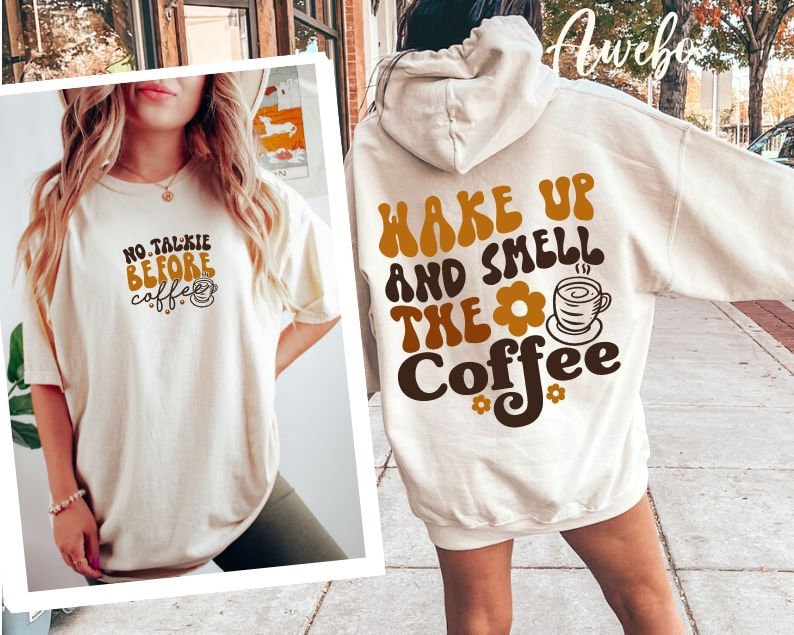 Może przedstawiać: Dwie białe koszulki z nadrukiem o tematyce kawy. Jedna koszulka ma napis "No Talkie Before Coffee" z grafiką kubka z kawą. Druga koszulka ma napis "Wake Up and Smell the Coffee" z grafiką kubka z kawą i kwiatem.