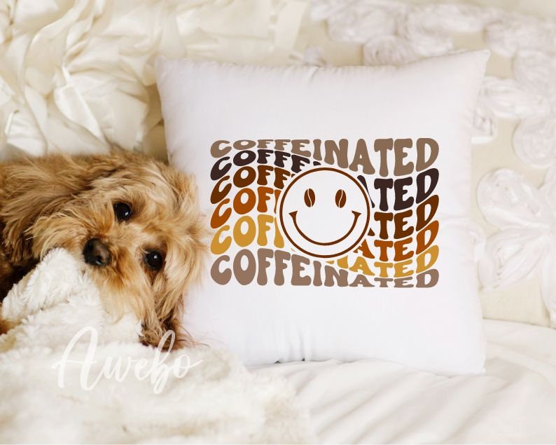 Może przedstawiać: Biała poduszka z brązowym i ż&oacute;łtym wzorem graficznym, na kt&oacute;rym widnieje napis "COFFEINATED" w retro czcionce z uśmiechniętą buźką w środku.
