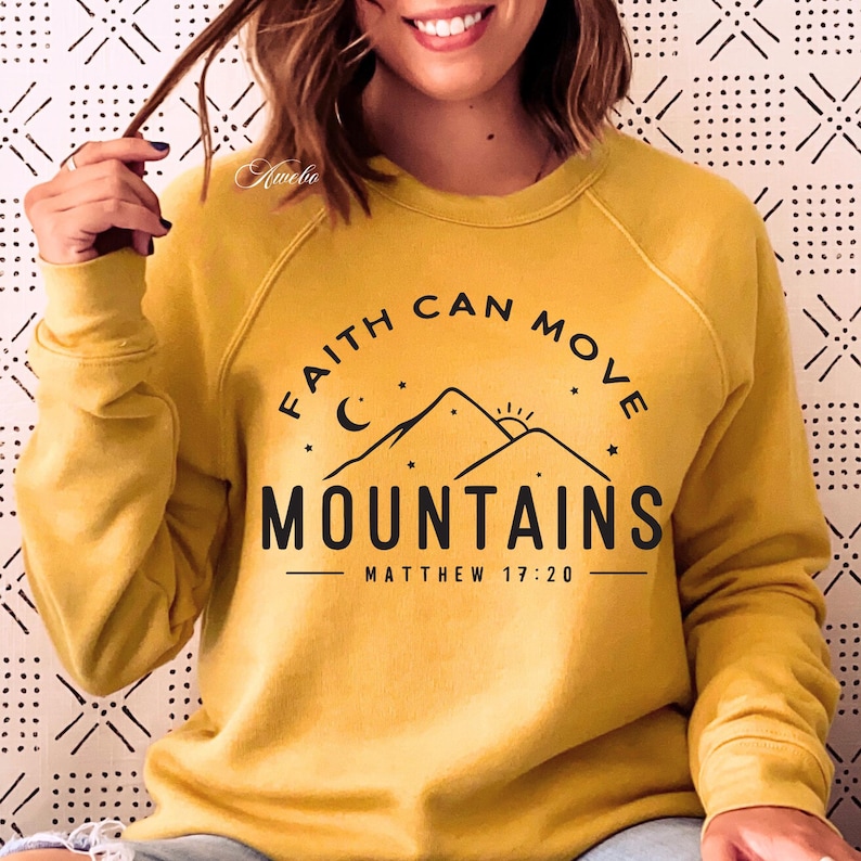 May include: Yellow sweatshirt with a black graphic that says "Faith can move mountains" with a mountain range, moon, and sun graphic. The text "Matthew 17:20" is also included.