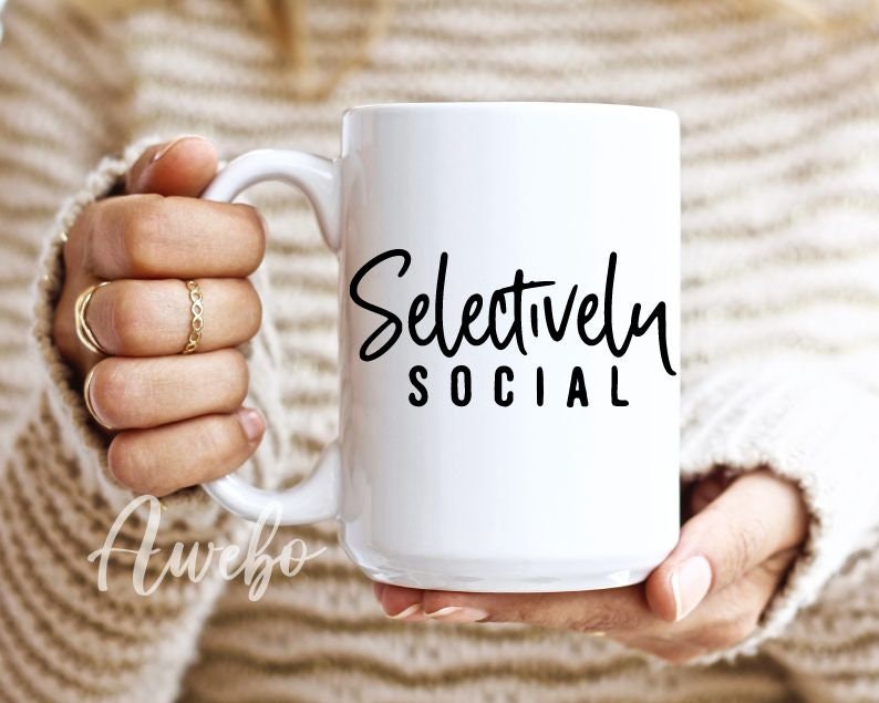 May include: White ceramic coffee mug with a black handwritten design that says "Selectively Social".