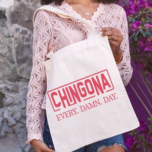 May include: A white tote bag with a red rectangle that says "CHINGONA" in all caps. Below the rectangle, it says "EVERY. DAMN. DAY."