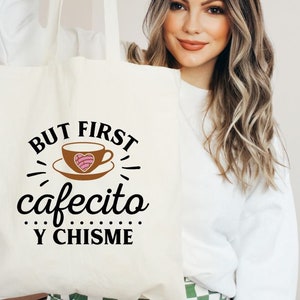 May include: White tote bag with black text that reads "But first, cafecito y chisme". The text is surrounded by a stylized coffee cup with a pink heart.