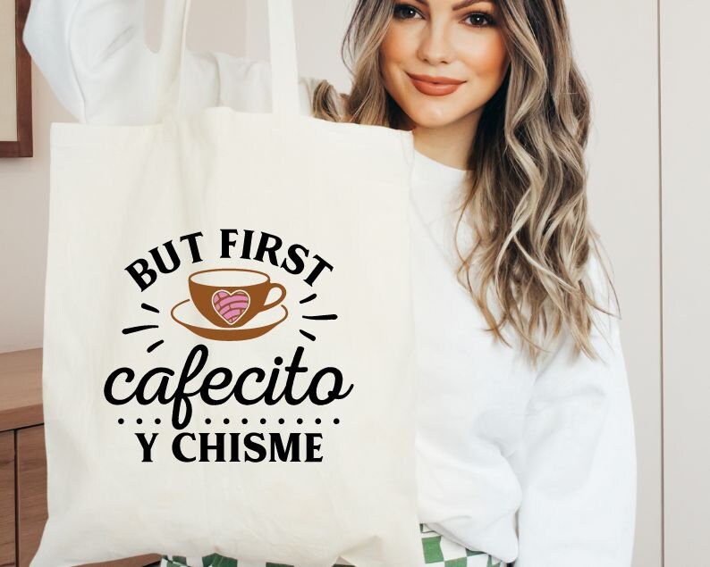 May include: White tote bag with black text that reads "But first, cafecito y chisme". The text is surrounded by a stylized coffee cup with a pink heart.