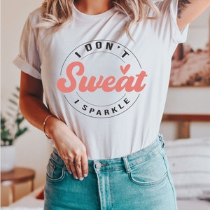 Pode incluir: Camiseta branca com um gr&aacute;fico circular preto que diz "I Don't Sweat I Sparkle" em uma fonte retr&ocirc; rosa.
